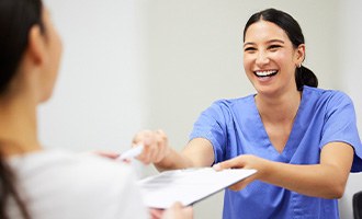 Woman in blue scrubs handing forms to patient