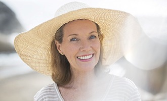 An older woman wearing a wide-brimmed hat and showing off her new and complete smile in Massapequa