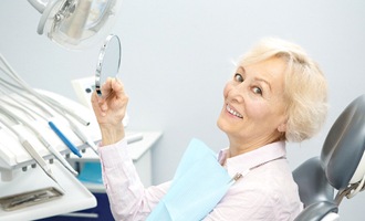 happy senior female dental patient admiring implant-supported teeth