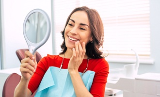 Woman smiling into hand mirror after full mouth reconstruction