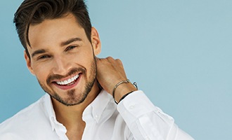 A young man wearing a white-button down shirt smiles after receiving his dental implants