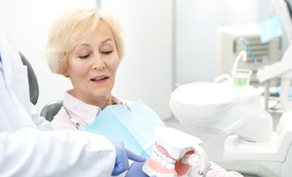 An older female patient listening as her dentist discusses her eligibility for implant dentures in Massapequa