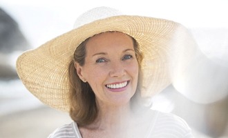 An older woman wearing a wide-brimmed hat and smiling after receiving her implant dentures in Massapequa