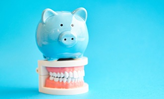 piggy bank atop model teeth for cost of dental implants in Massapequa Park
