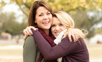 A mother and daughter hugging outside.