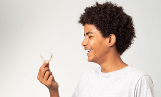 Teenage boy smiling while holding clear aligner