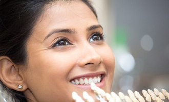 A young female smiling while a dentist uses a shade guide to determine the color of her new veneers