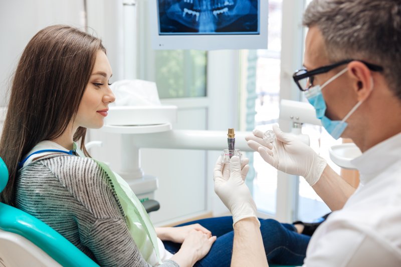 a dentist showing a female patient how a dental implant works