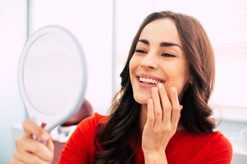 a young woman wearing a red blouse and admiring her smile after receiving dental implants