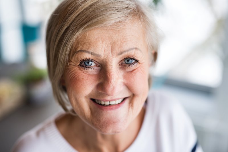 Older woman in white shirt smiling with implant dentures