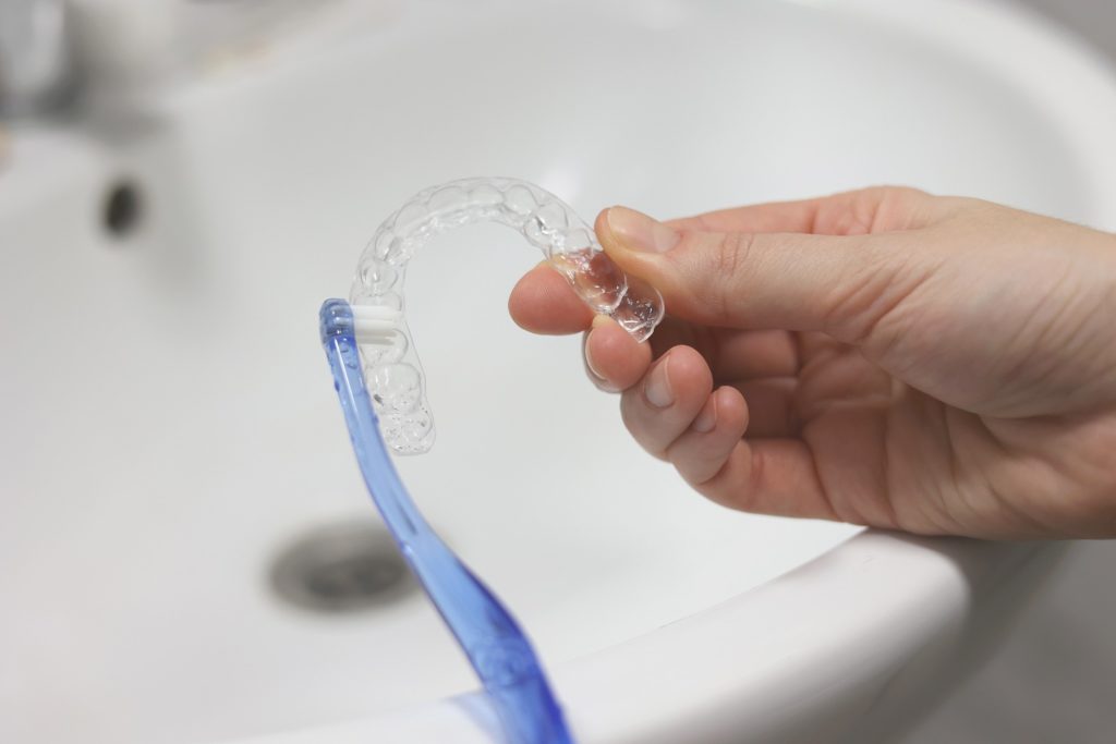 Patient using toothbrush to clean their Invisalign aligners