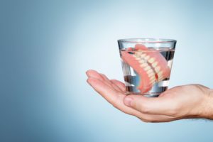 Hand holding a glass of water containing dentures