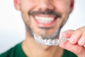 Man smiling while holding an Invisalign clear aligner