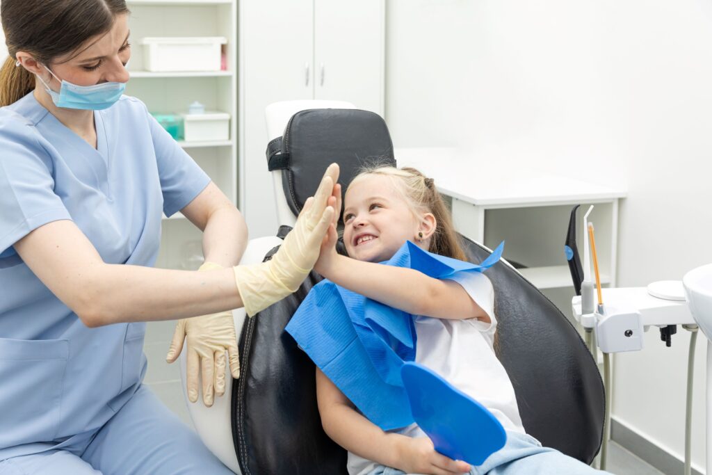 Little girl in dental chair high-fiving dentist